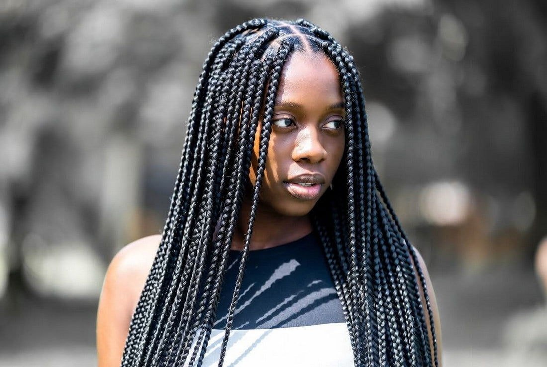 Young Black woman with long, thick black knotless box braids looking away from the camera.