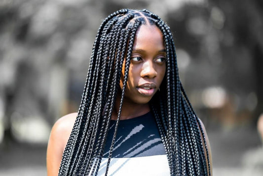 Young Black woman with long, thick black knotless box braids looking away from the camera.