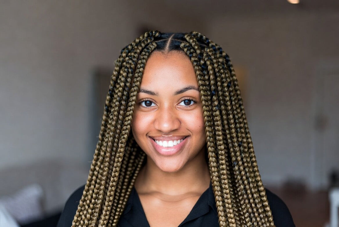 Smiling young woman with long, neatly done blonde-highlighted knotless box braids looking at the camera.