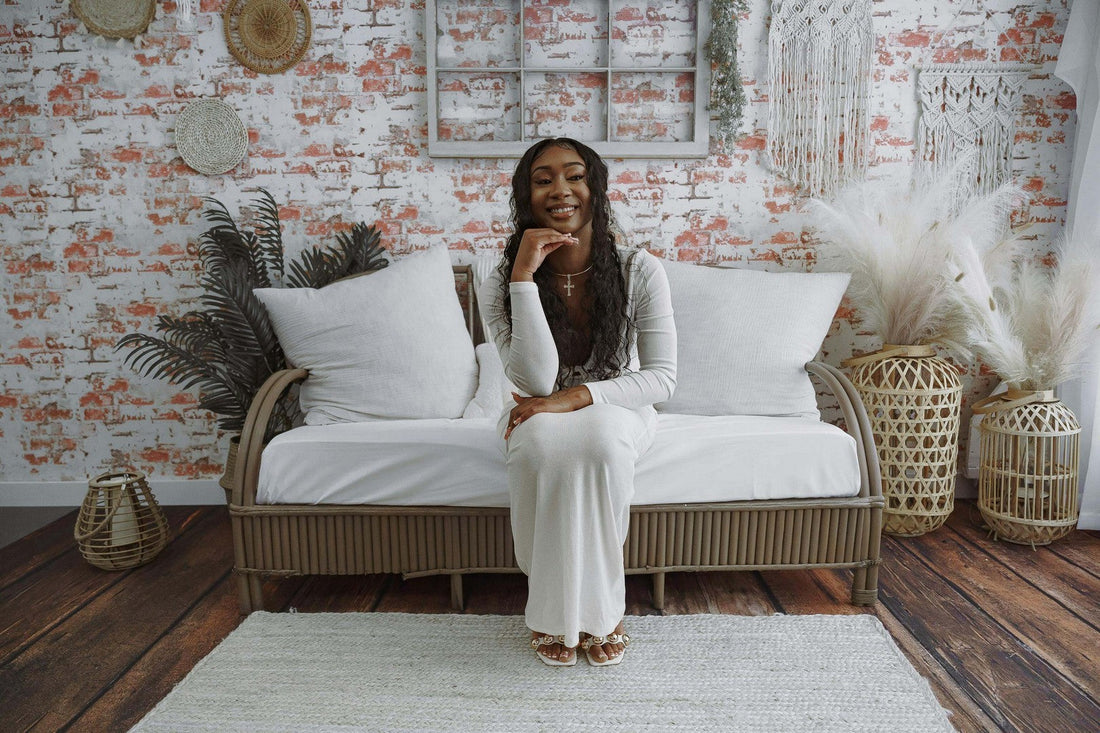 Beautiful Black woman with long boho knotless braids sitting on a white sofa in a boho-style studio interior.