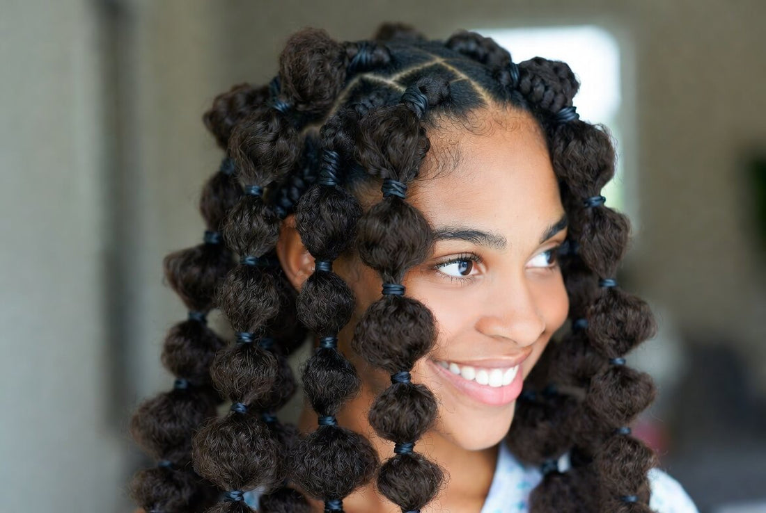 Radiant portrait of a smiling woman with long goddess braids — a mix of cornrows and loose voluminous curls with gold beads. She has a joyful expression and is looking slightly to the side outdoors.