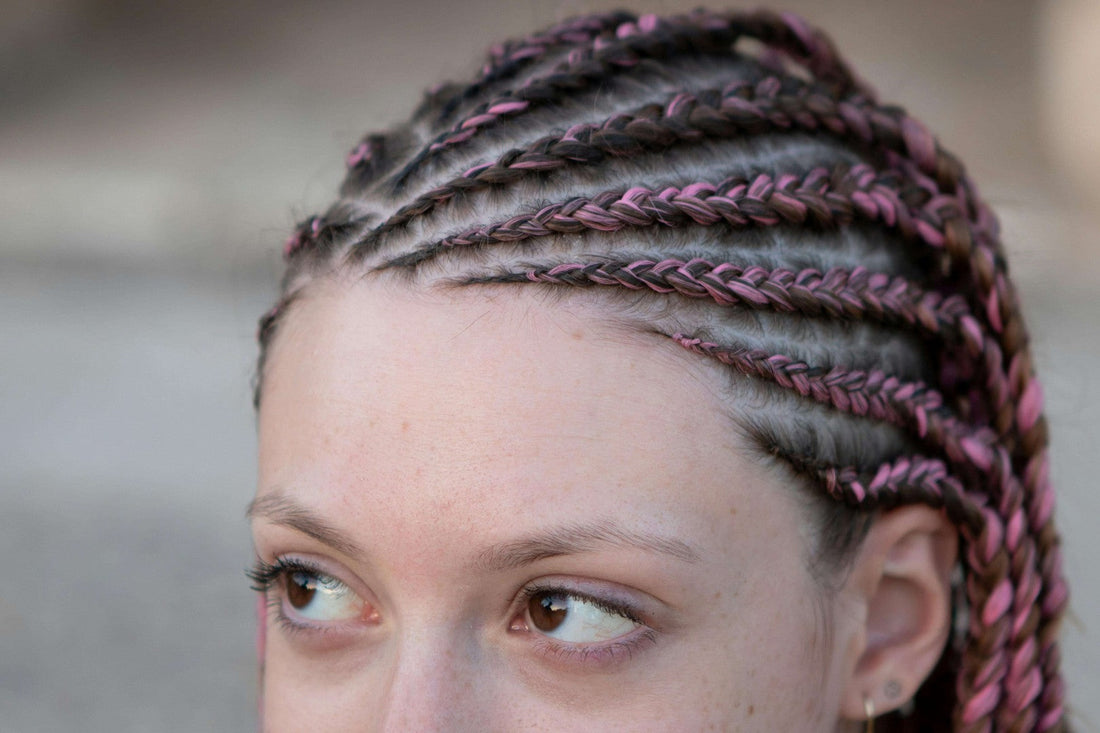 Close-up of a woman with stylish half-up half-down braids featuring pink accents and intricate braiding pattern.