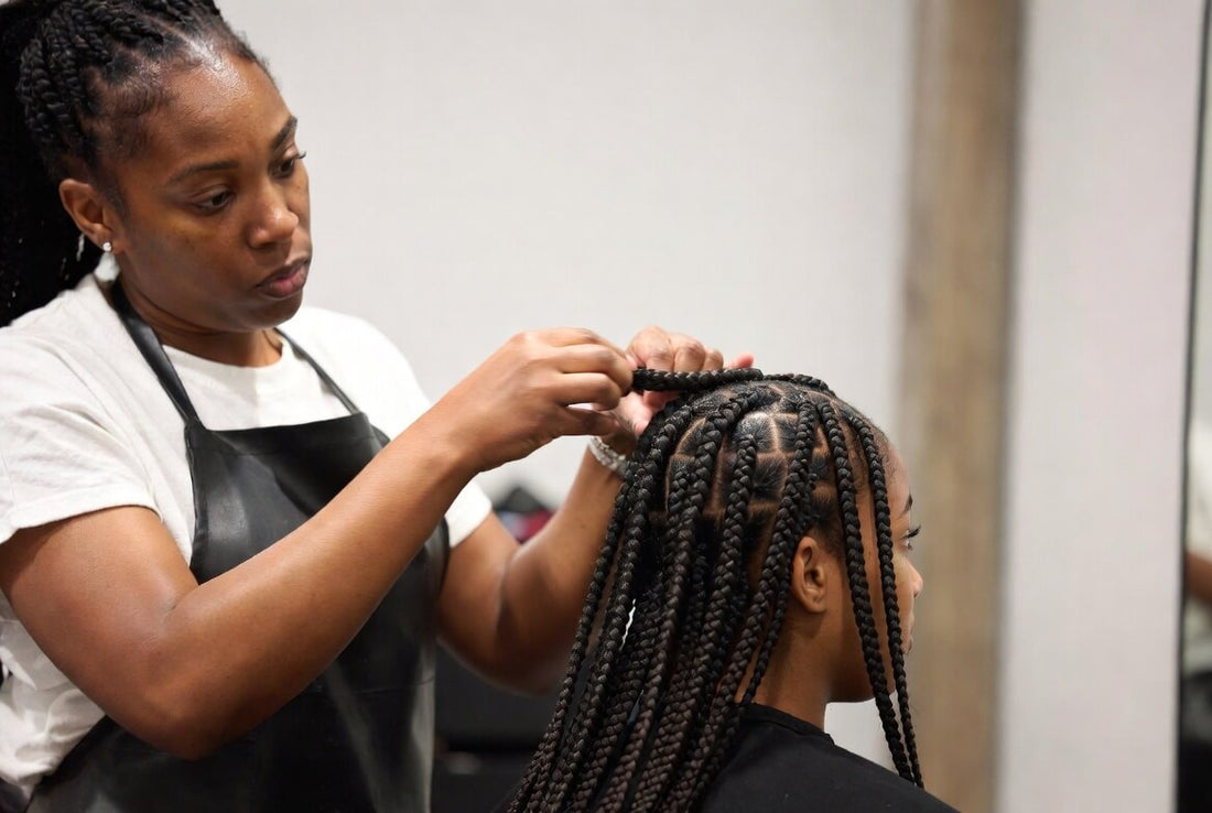 Professional hairstylist carefully installing knotless box braids on a client in a salon.