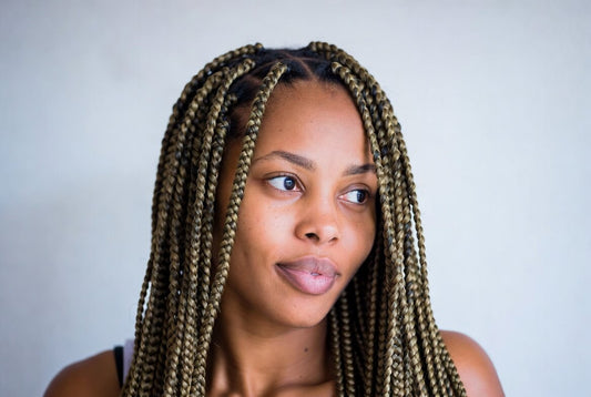 Close-up portrait of a young woman with long blonde-highlighted box braids looking to the side.
