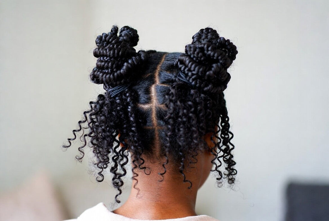 Back view of a child with natural black hair styled in two high bubble buns (puffs) with a neat grid parting. The rest of the hair falls in defined curly twists — a classic protective hairstyle.