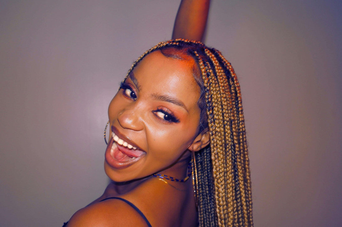 Cheerful woman with small box braids smiling playfully with her tongue out, wearing hoop earrings.