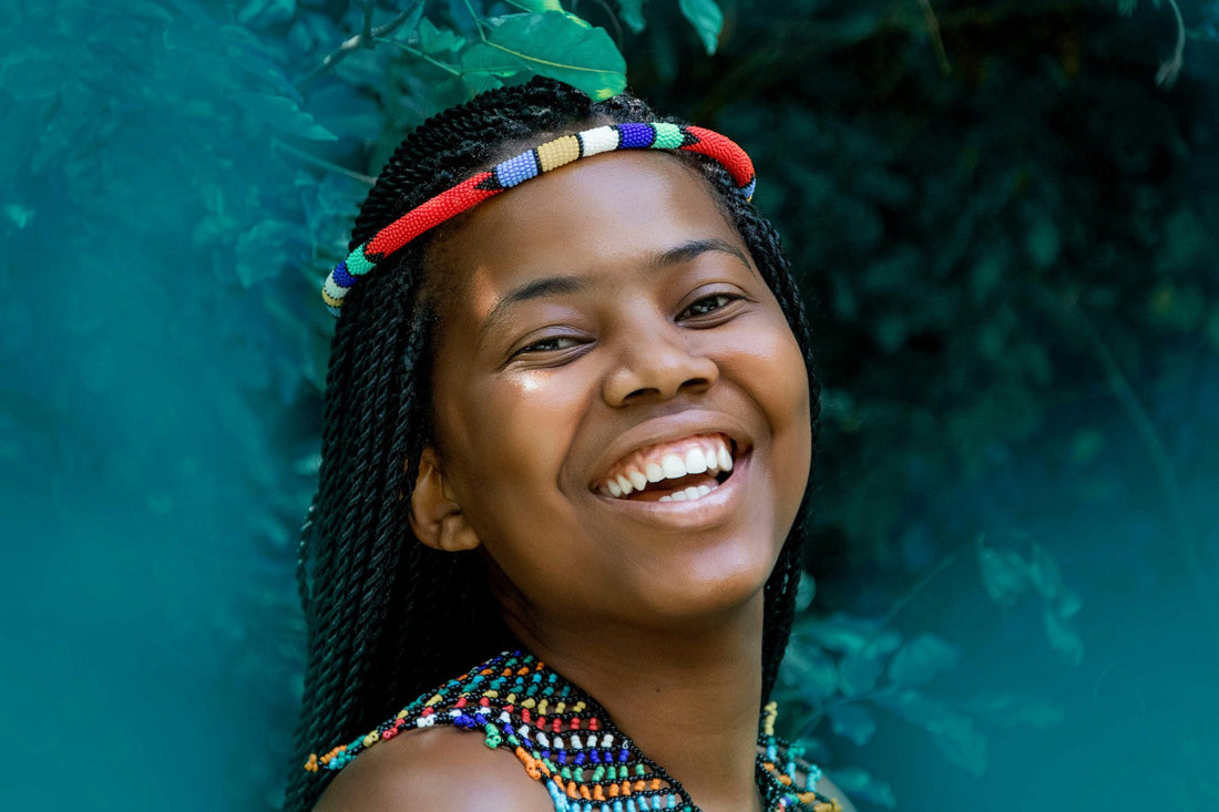 Happy young woman with traditional tribal braids wearing a colorful beaded headband and necklace, smiling outdoors.